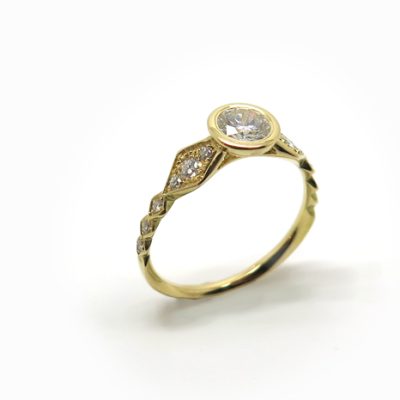 Solitaire en or jaune dont le corps de bague est très travaillé et pavé de diamants